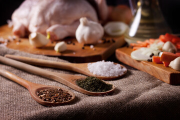 Dried dill, sea salt and seasoning of dried vegetables and spices with Basil on wooden tablespoons on the background of chicken and vegetables prepared for cooking