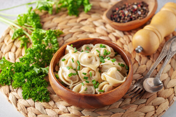 Fototapeta na wymiar Homemade meat dumplings with onions and parsley- russian pelmeni in wooden bowl.
