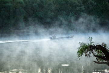 morning evaporation of water over the river, powerboat floats on the river through the fog