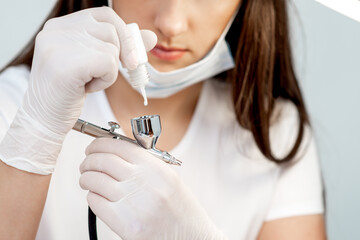 Manicure master adds white paint to airbrush before before the spraying procedure in nail salon