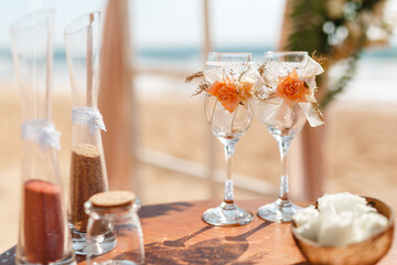 Wedding glasses decorated with ribbon and flowers on the table, ocean on background. Wedding by the sea