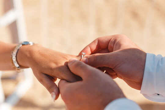 Romantic marriage proposal on the beach at the seaside. Groom wearing the diamond ring to bride hand close up