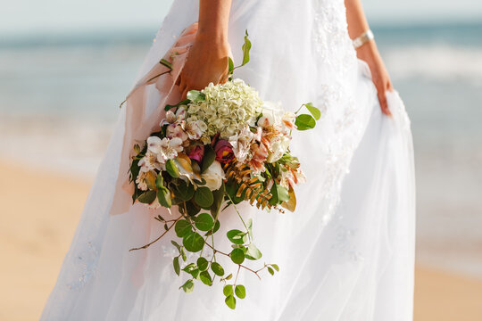 Cropped image bride in wedding dress hold in hands bouquet of tropical flowers on the background of the sea