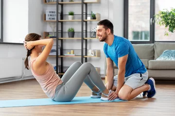 Fotobehang fitness, sport, training and healthy lifestyle concept - woman with personal trainer doing sit ups at home © Syda Productions