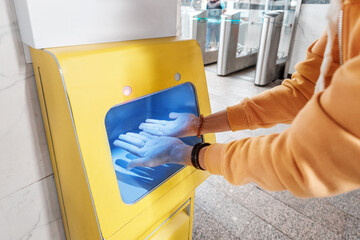 Passenger disinfects and washes hands in a special device with a sanitizer at the public transport station.