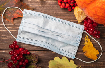 Medical protective mask on an autumn background. Pumpkin, red berries, on a wooden background with...