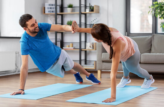 fitness, sport, training and healthy lifestyle concept - happy couple make high five in side plank at home