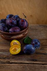 Blue plum in a bowl on a wooden table. Plums in a cut. Top view, place for text. Fruit background with copy space. Still life food.