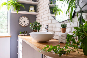 Bathroom interior with window, stylish sink on wooden counter, green plants and mirror on white...