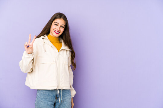 Young caucasian woman isolated on purple background joyful and carefree showing a peace symbol with fingers.
