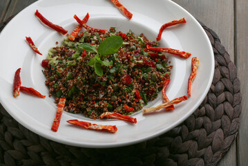 Red quinoa salad with dry tomato slices on wicker table mat