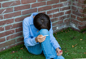 A sad boy is sitting on the street alone holding a cigarette and lighter. Unhappy lonely child. family issues teen problem