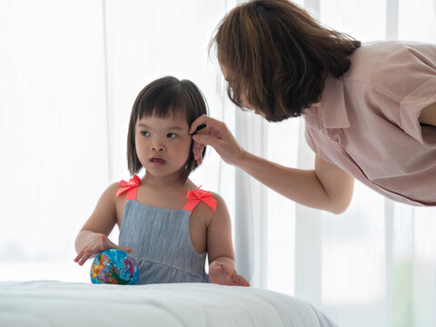 Asian Mother Talking To Young Little Down Syndrome Daughter Softly While She Plays With Global Toy Ball. Happy Family With Special Needs Child Concept.