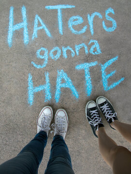 Two kids standing above chalk words that say Haters gonna Hate