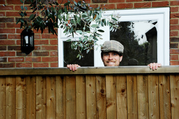 Nosy neighbor peeking over the fence, spying on his neighbours during the covid-19 lockdown