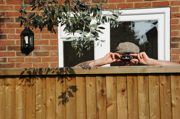 Nosy neighbor peeking over the fence, spying on his neighbours during the covid-19 lockdown - obrazy, fototapety, plakaty
