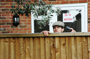 Nosy neighbor peeking over the fence, spying on his neighbours during the covid-19 lockdown