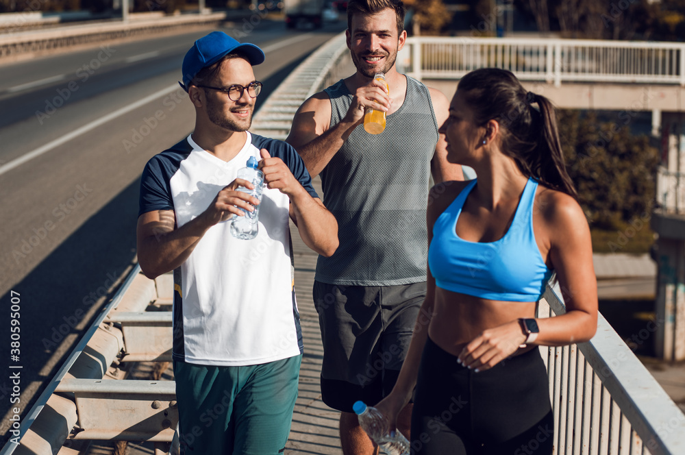 Wall mural Group of young people in sports clothing running in city street in morning.