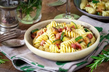 Delicious Italian fusilli pasta with zucchini or courgette and pancetta served in a vintage plate on a dark rustic wooden background - obrazy, fototapety, plakaty