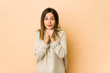 Fototapeta premium Young woman isolated on beige background praying for luck, amazed and opening mouth looking to front.