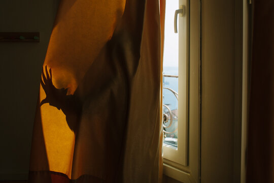 Shadow hand of child hiding behind curtain.