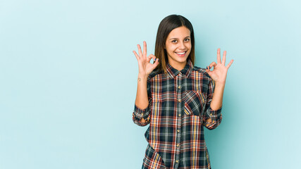 Young woman isolated on blue background cheerful and confident showing ok gesture.