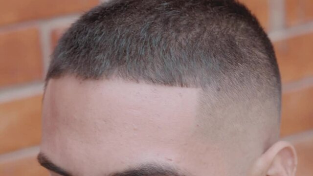 Barbero utilizando maquina de afeitar y peine para marcar frente de modelo masculino en peluquer&iacute;a 