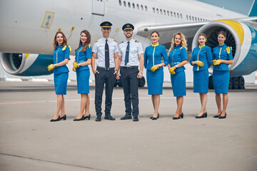 Handsome pilots and beautiful stewardesses standing outdoors in airfield