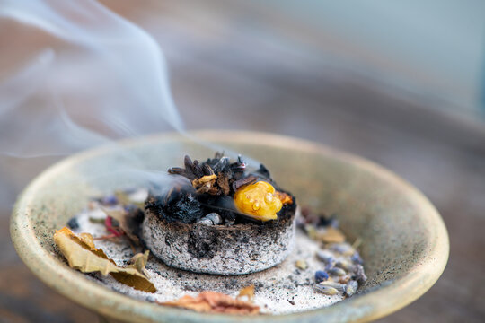 Nahaufnahme: Weihrauch und getrocknete Bl&uuml;ten und Kr&auml;uter verbrennen bei einem R&auml;ucherritual auf einer gl&uuml;henden R&auml;ucherkohle