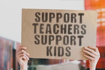 The phrase " Support teachers support kids " on a banner in men's hand with blurred background. Education. Schools. Knowledge. Crisis. Occupation. Profession. Job. Tutor