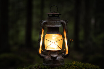 Old vintage lantern lit in the darkness close up. Blurred background image of a glowing lantern.