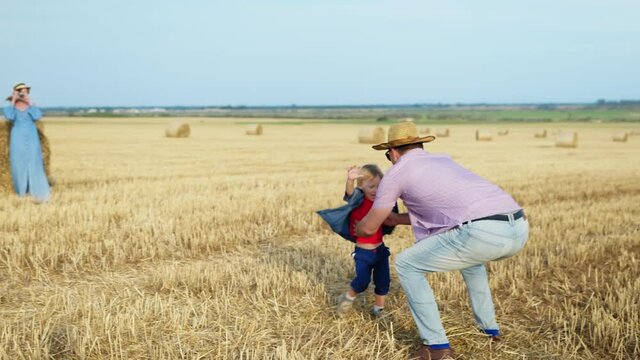 happy infancy, caring father plays his little son and throws child up in blue sky during family vacation in field after harvest background of haystacks