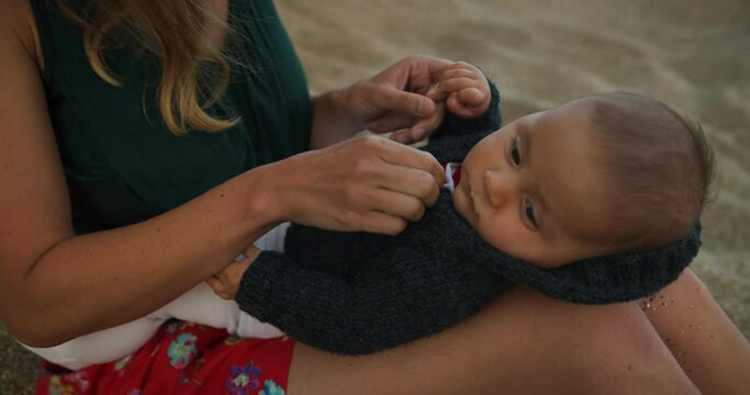 A young mother on the beach at sunset is putting a cardigan on her baby