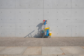 Wagen mit Putzmitteln vor Betonwand im Sonnenlicht.