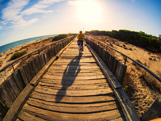 Una mujer pasea en biccleta por un camino de madera junto a la playa al atardecer en Huelva.