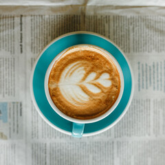Top view of coffee art on foam of delicious latte in cup placed on newspaper in cafe in morning 