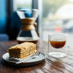 Sweet honey cake and glass cup of chemex coffee arranged on wooden table in cozy cafe in morning