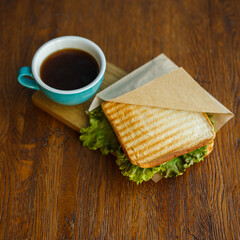 From above of appetizing sandwich placed on wooden table with cup of brown coffee for breakfast in morning   