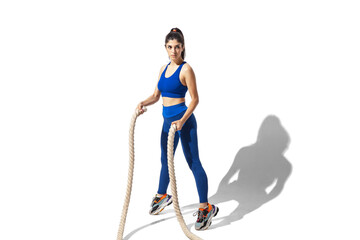 Ropes. Beautiful young female athlete practicing on white studio background, portrait with shadows. Sportive fit model in motion and action. Body building, healthy lifestyle, style concept.