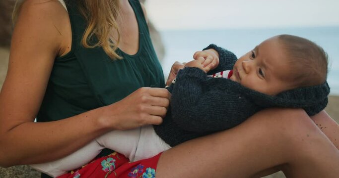 A young mother on the beach at sunset is putting a cardigan on her baby