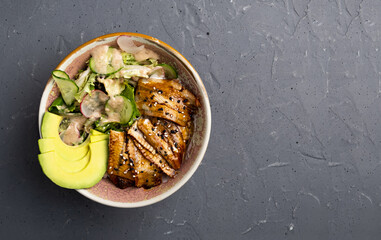Hawaiian dish. Poke salad with eel, rice and avocado in a deep bowl on a gray background. The view from the top. No people. Copy space