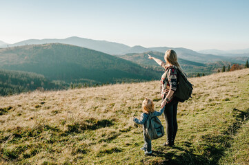 Mom with backpack and child walk in autumn grass. The daughter and mother walking on nature. Family...