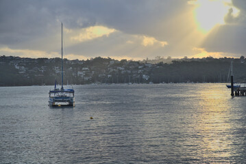 Fototapeta premium Yacht in water at sunset against a background of Manly cove marine and rural houses, Manly, New South Wales, Australia
