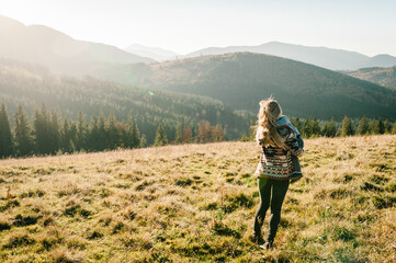 Fototapeta premium Mother with kid hiking in mountains. Young tourists on top of a mountain enjoying valley view before sunset. Happy family mom kissing and hugging daughter.
