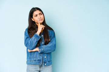Young indian woman isolated on blue background looking sideways with doubtful and skeptical...