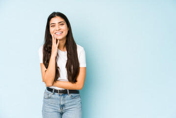 Young indian woman on blue background laughs happily and has fun keeping hands on stomach.