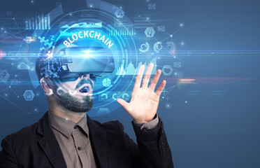 Businessman looking through Virtual Reality glasses with BLOCKCHAIN inscription, innovative technology concept