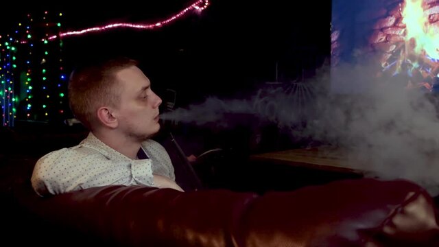 Side view of a man in relaxing atmosphere exhaling white thick smoke from his mouth. Media. Concept of nightlife and bad habit, male spending time at night bar.