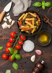 Fusilli pasta in black bowl with parmesan cheese and tomatoes, oil and garlic with basil and linen towel on wooden background.