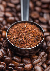 Fresh raw organic ground coffee powder in black steel scoop on top of coffee beans.
